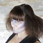 Female model with dark brown hair puffed out with glitter highlights in alien makeup on her face