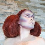 Female model with red hair puffed out with small braid details in alien makeup on her face