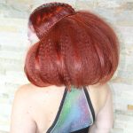 Female model with red hair puffed out with small braid details in alien makeup on her back